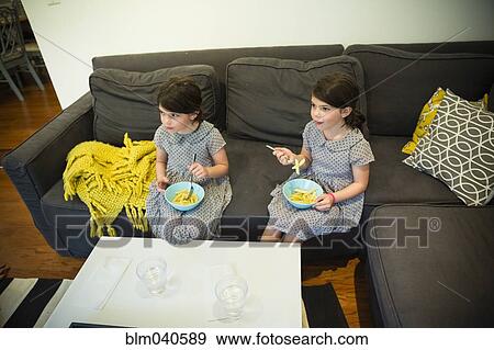 Twin sisters eating on sofa View Large Photo Image Stock Photo - Twin sisters eating on sofa. Fotosearch