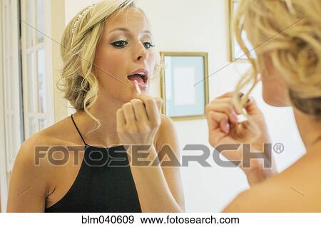 Stock Photo - Woman applying lip gloss in mirror. Fotosearch