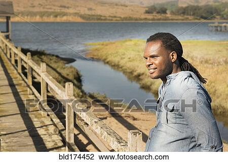 Stock Image - African American man standing on wooden deck. Fotosearch