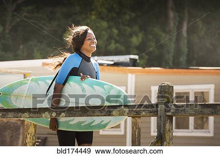 Stock Photo - African American woman carrying surfboard outdoors. Fotosearch