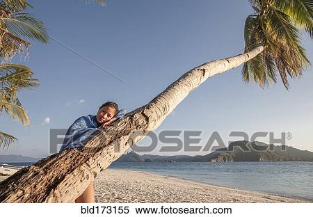Stock Photography - Asian woman on palm tree on beach. Fotosearch