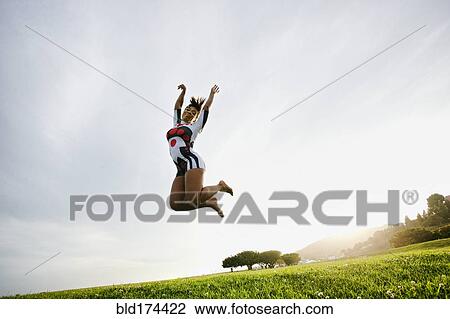 Stock Image - Black woman jumping for joy in field. Fotosearch