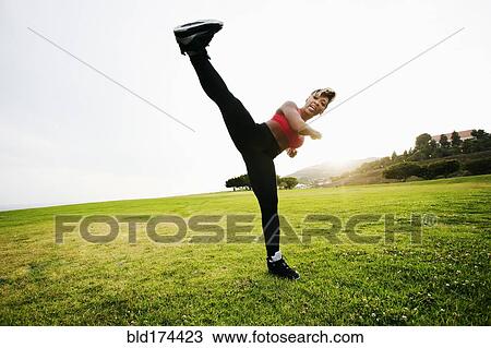 Stock Image - Black woman kick boxing in field. Fotosearch