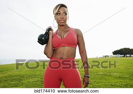 Stock Image - Black woman lifting weights in field. Fotosearch