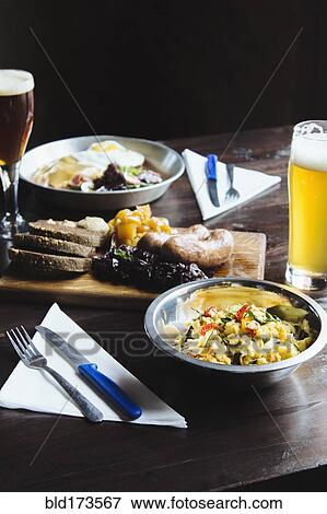 Stock Photo - Bowl of pasta, cheese on cutting board and beer on table. Fotosearch