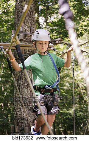 Stock Image - Caucasian boy balancing on rope bridge. Fotosearch