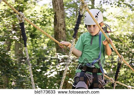 Stock Image - Caucasian boy balancing on rope bridge. Fotosearch