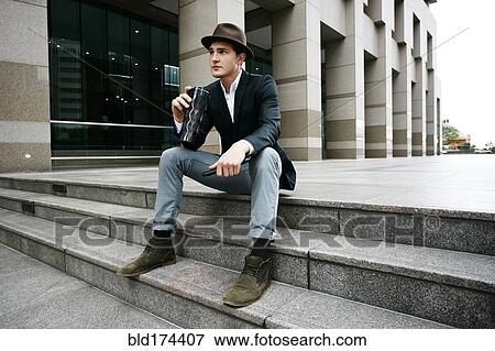 Stock Photo - Caucasian businessman drinking coffee on steps. Fotosearch