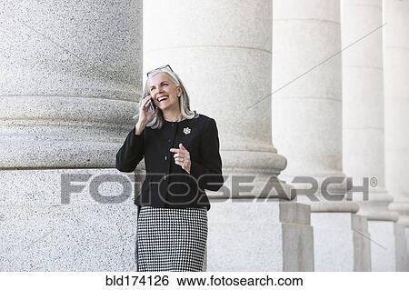 Stock Photograph - Caucasian businesswoman talking on cell phone under columns. Fotosearch