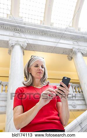 Stock Image - Caucasian businesswoman using cell phone in courthouse. Fotosearch