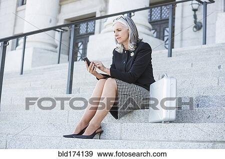 Stock Photo - Caucasian businesswoman using cell phone on courthouse steps. Fotosearch