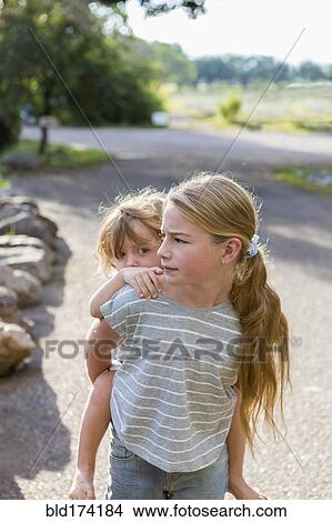Picture - Caucasian girl carrying toddler brother piggyback. Fotosearch