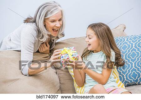 Stock Photo - Caucasian girl giving grandmother a gift in living room. Fotosearch