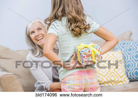 Stock Photograph - Caucasian girl hiding gift for grandmother behind back. Fotosearch