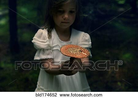 Stock Image - Caucasian girl holding mushroom in forest. Fotosearch