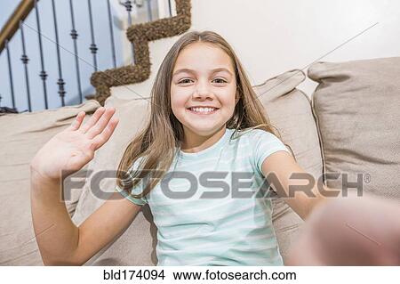 Picture - Caucasian girl taking selfie on sofa. Fotosearch