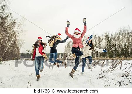 Stock Image - Caucasian girls jumping for joy in snow. Fotosearch