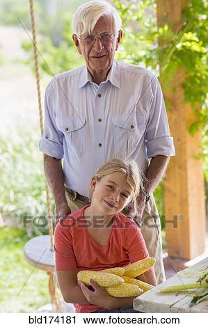 Stock Image - Caucasian grandfather and granddaughter shucking corn. Fotosearch