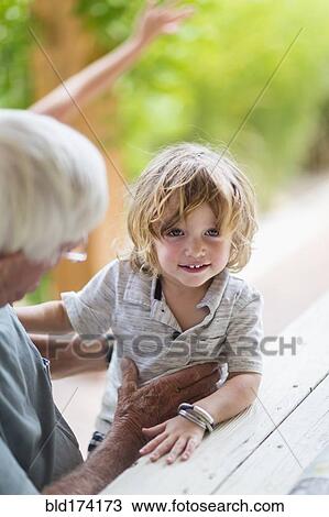 Stock Image - Caucasian grandfather and grandson sitting at table. Fotosearch