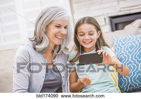 Stock Image - Caucasian grandmother and granddaughter listening to cell phone. Fotosearch
