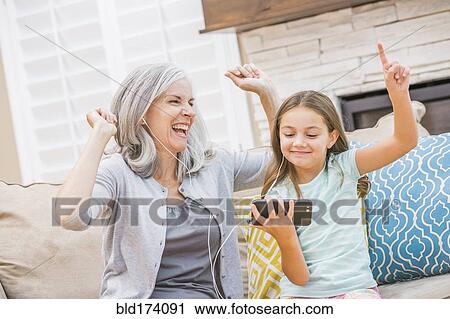 Stock Image - Caucasian grandmother and granddaughter listening to cell phone. Fotosearch