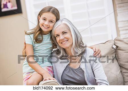 Stock Image - Caucasian grandmother and granddaughter hugging on sofa. Fotosearch