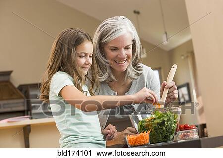 Stock Image - Caucasian grandmother and granddaughter making salad in kitchen. Fotosearch