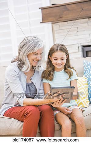 Stock Photo - Caucasian grandmother and granddaughter using digital tablet on sofa. Fotosearch