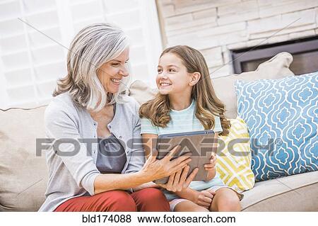Stock Photo - Caucasian grandmother and granddaughter using digital tablet on sofa. Fotosearch