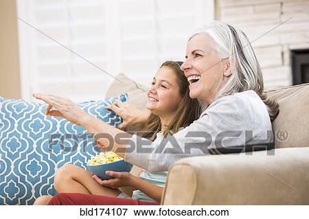 Stock Photo - Caucasian grandmother and granddaughter watching television on sofa. Fotosearch