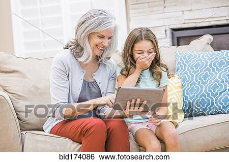 Stock Photograph - Caucasian grandmother and granddaughter using digital tablet on sofa. Fotosearch