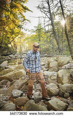 Stock Image - Caucasian man fishing in forest steam. Fotosearch