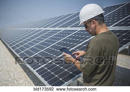 Stock Image - Caucasian technician using digital tablet near solar panels. Fotosearch