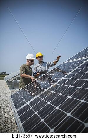 Stock Photo - Caucasian technicians examining solar panels. Fotosearch