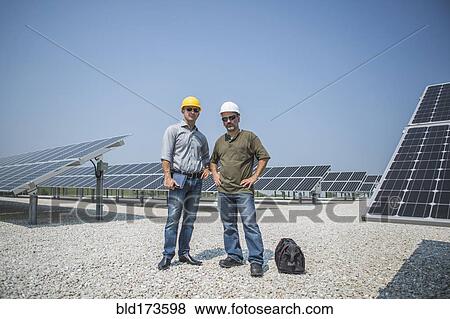 Stock Photo - Caucasian technicians standing near solar panels. Fotosearch