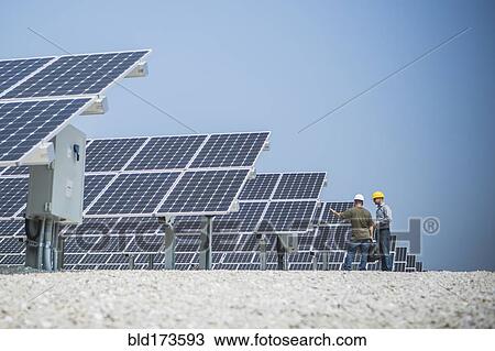 Stock Image - Caucasian technicians talking near solar panels. Fotosearch