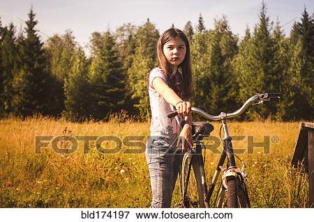 Stock Photo - Caucasian teenage girl pushing bicycle in field. Fotosearch