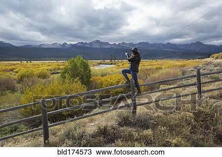 Stock Image - Caucasian woman photographing rural river. Fotosearch