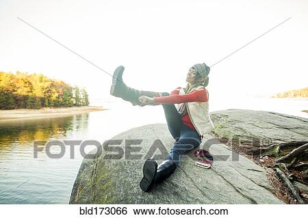Stock Photograph - Caucasian woman pulling on boots near lake. Fotosearch