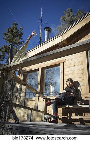 Picture - Caucasian woman reading book on cabin porch. Fotosearch