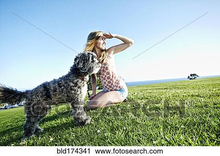 Stock Image - Caucasian woman sitting in field with dog. Fotosearch