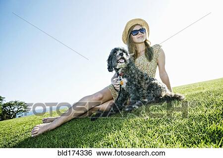 Stock Photograph - Caucasian woman sitting in field with dog. Fotosearch