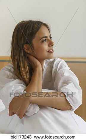 Stock Image - Caucasian woman sitting on bed. Fotosearch