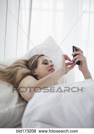 Stock Photo - Caucasian woman using cell phone in bed. Fotosearch