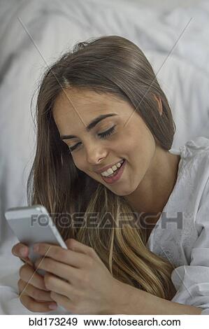 Stock Photo - Caucasian woman using cell phone in bed. Fotosearch