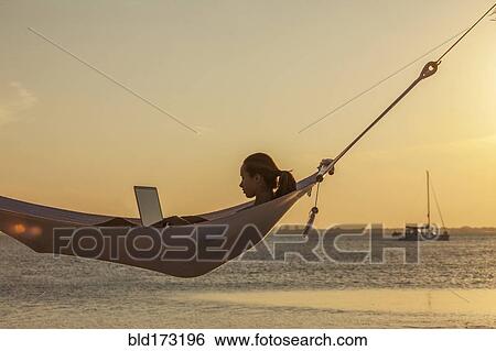 Stock Photograph - Caucasian woman using laptop in hammock. Fotosearch