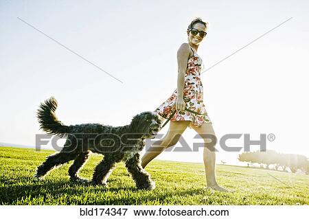 Stock Photo - Caucasian woman walking dog in field. Fotosearch