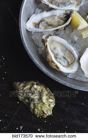 Stock Image - Close up of oysters and lemon on ice. Fotosearch