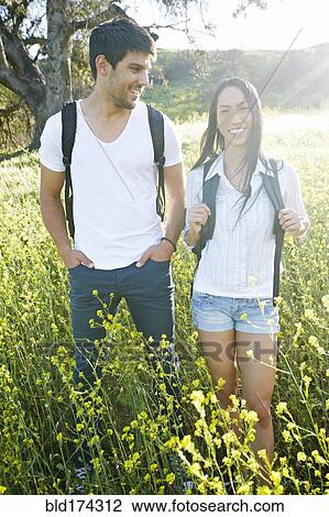Stock Image - Couple carrying backpacks in field. Fotosearch