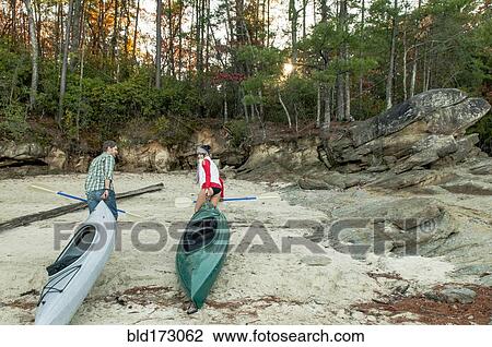 Stock Image - Couple pulling kayaks on rocks. Fotosearch